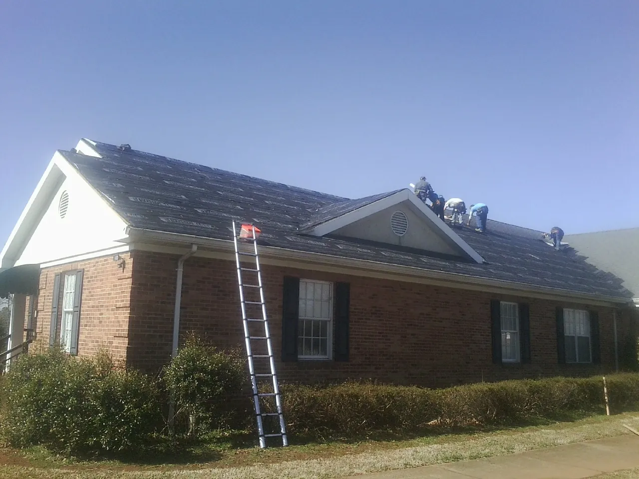 Crew tearing shingles off a brick ranch roof with a ladder set — Emergency Roof Repair work by our crew in West Nyack