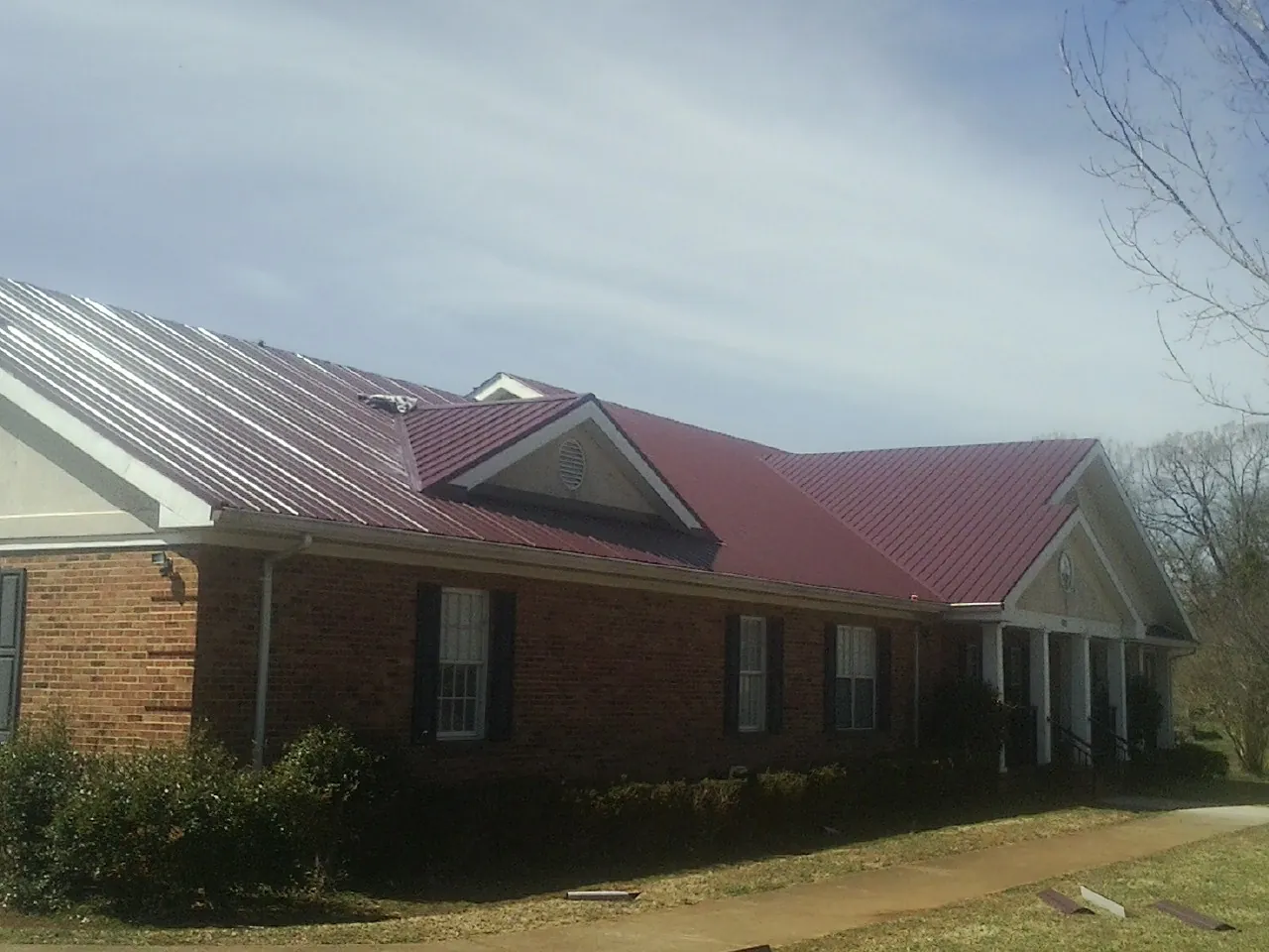 Red metal roof with gabled entries on a long brick building, from a Hail Damage Roof Repair job in West Nyack