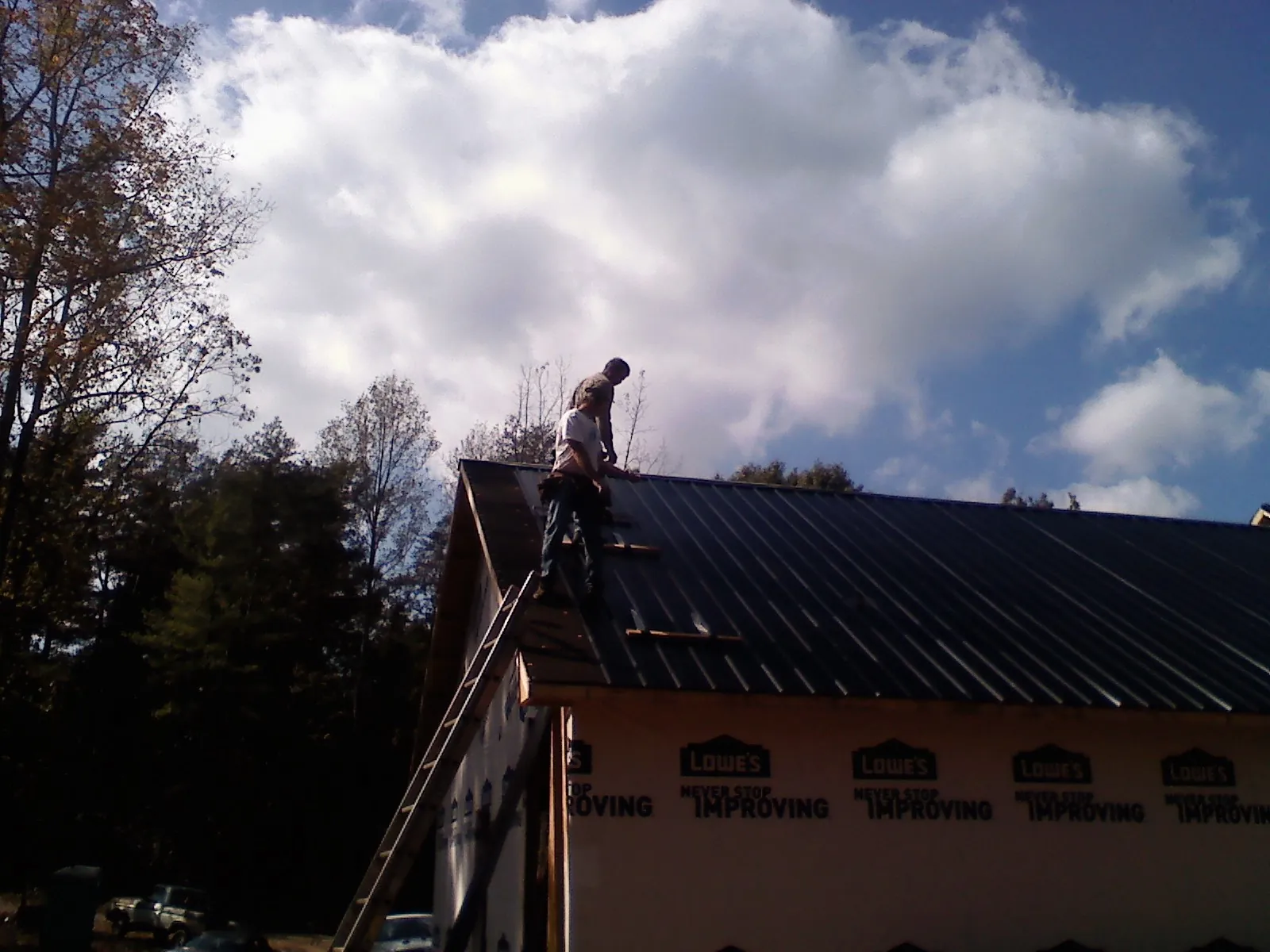 Roofer fastening dark metal panels high against a cloudy sky, from a Roof Inspection job in West Nyack