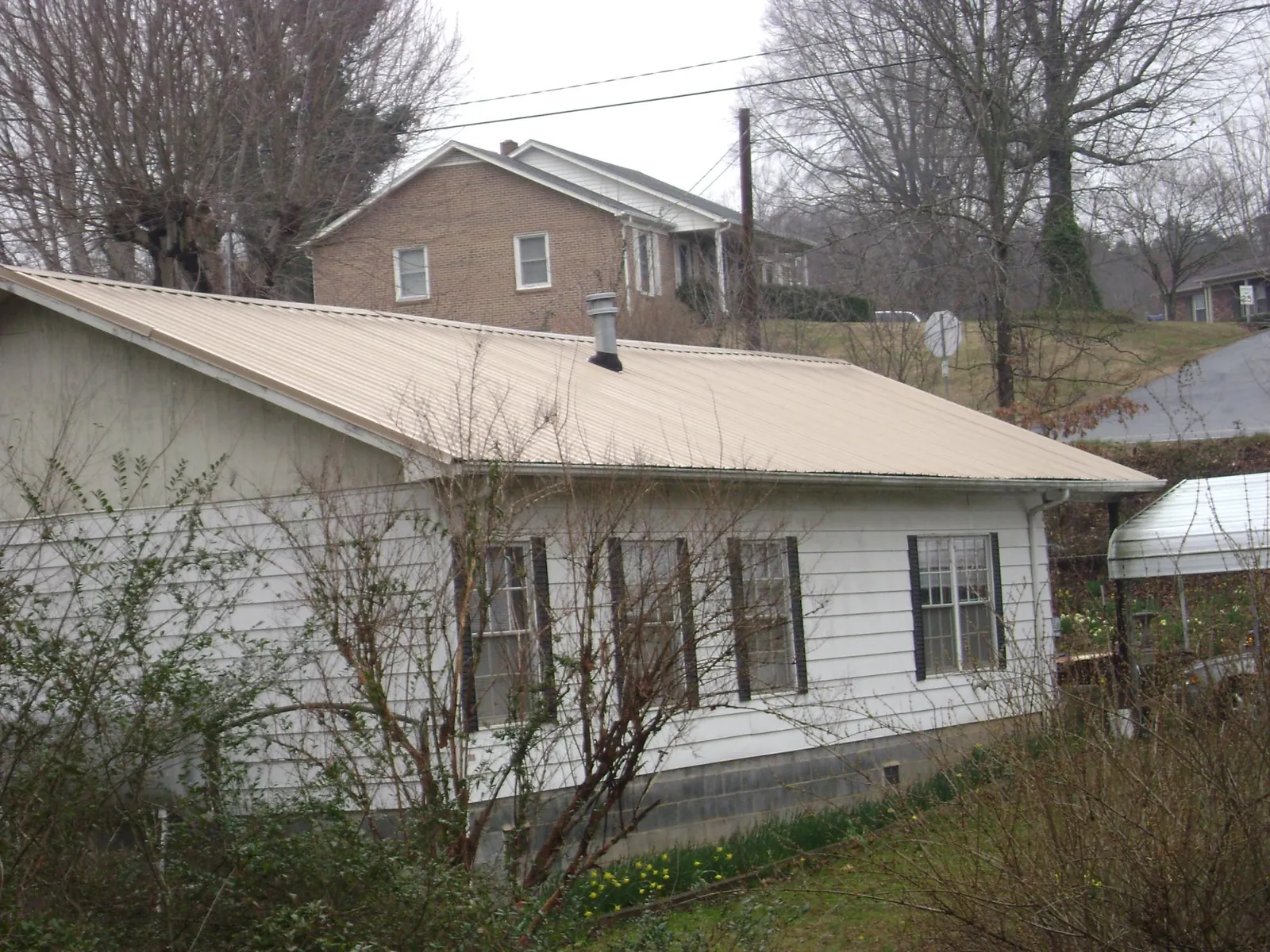 Tan metal roof on a white sided house set into a hillside — Commercial Roofing by Roofing Brothers in West Nyack